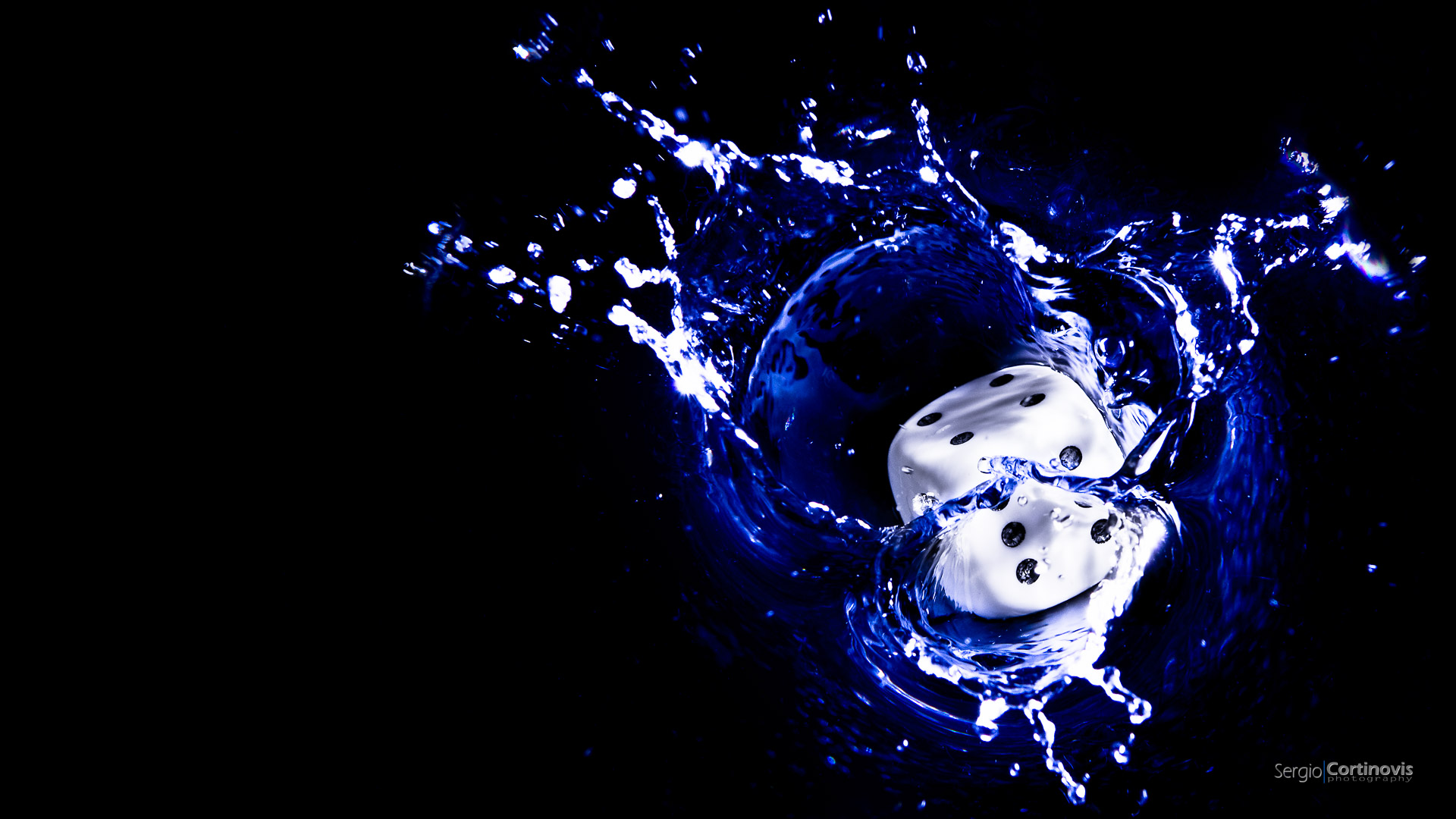 Un dado bianco cade nell'acqua resa nera tramite l'utilizzo del flash