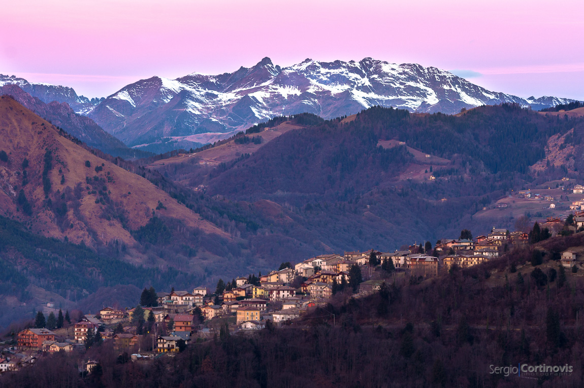 Fotografia di Costa Serina all'alba con cielo rosa e montagne con la neve