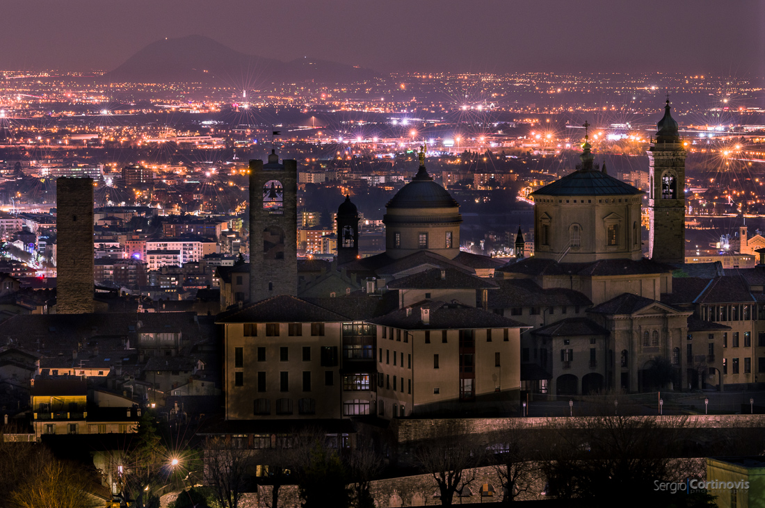 Città Alta al buio di notte davanti a Bergamo bassa illuminata: questo è M'illumino di meno