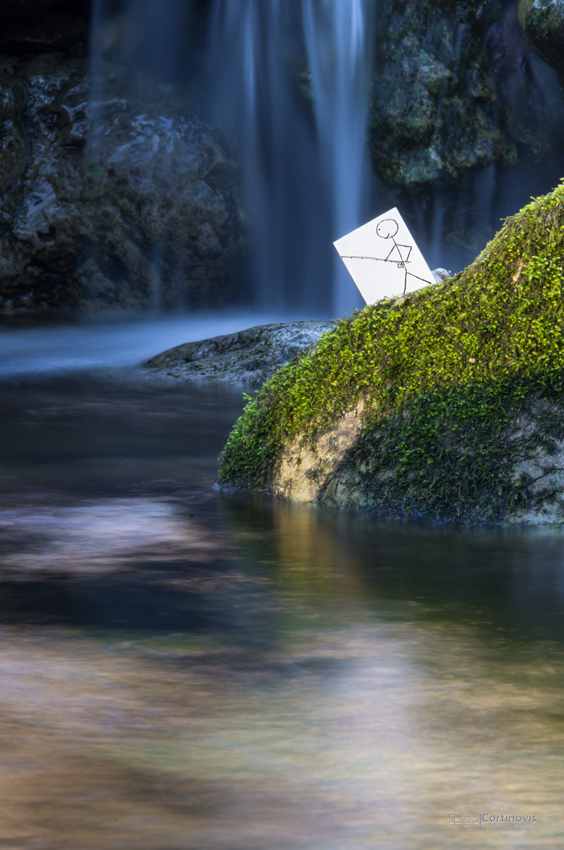 Un pescatore di carta di fronte ad una cascata d'acqua dalle proporzioni particolari. Fotografia realizzata a Cornalba