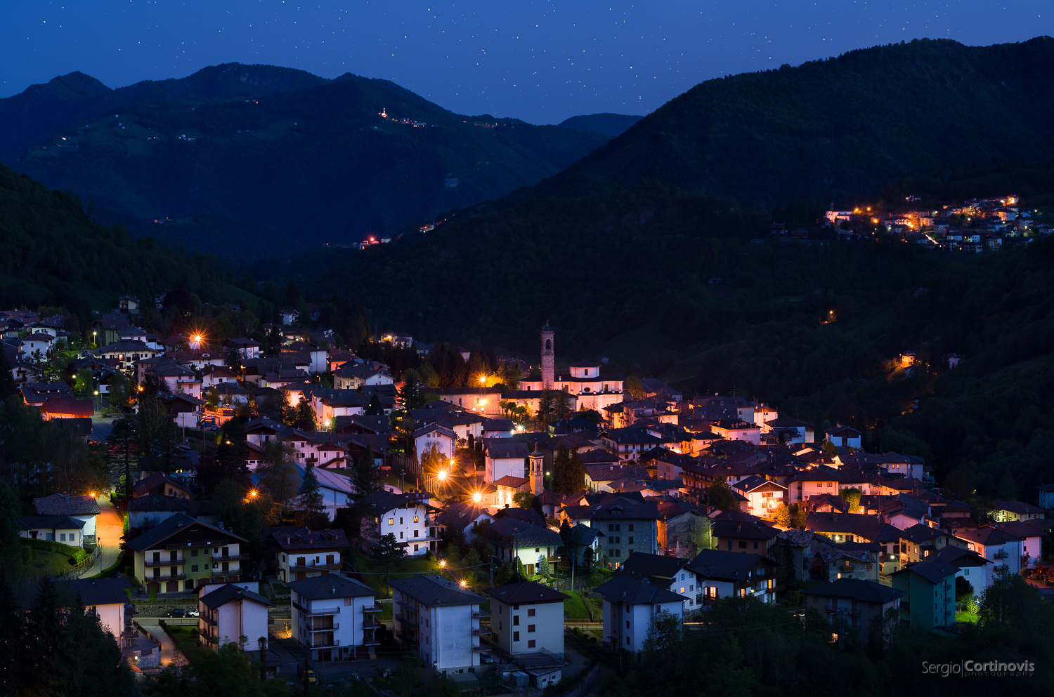 Serina di notte vista dalla strada che porta a Valpiana. Si vede la chiesa parrocchiale e sullo sfondo Lepreno.