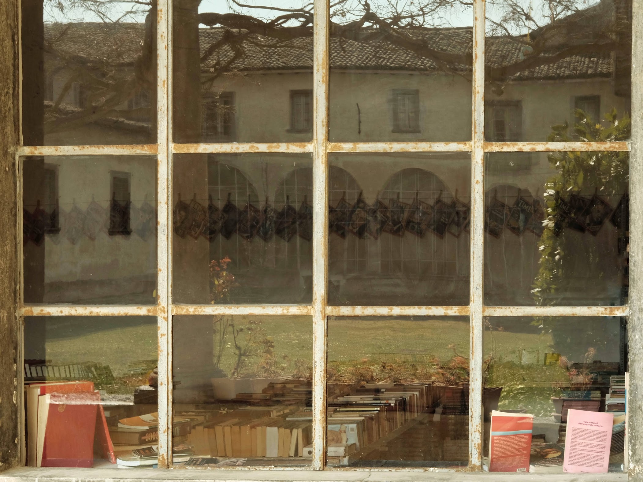 Libri di una biblioteca visti attraverso un'ampia finestra, nella quale si rispecchia il chiostro del convento di Serina
